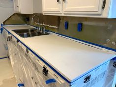 a kitchen with white cabinets and blue tape around the counter tops that are being installed