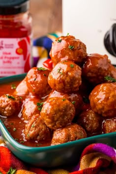 meatballs with sauce and parsley in a green bowl on a colorful cloth next to a jar of ketchup