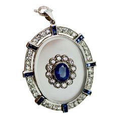 This is part of Chairish’s Fine Jewelry assortment.  Rock Crystal Pendant Sapphire Diamonds 18K  I just love this pendant. This pendant is beautiful with a frosted Rock Crystal base set with a Sapphire with Diamond surround. The crystal is set with Diamonds and Sapphires on a simple chain. The center stone is 0.75 carats, each baguette stone is 0.35 carats and have a Diamond surround of 12 Diamonds. Total Diamond weight is 1.16 carats, Sapphires 1 carat. Weights 0.76 grams. Entire piece 3 CM. We White Gold Jewelry With Large Oval Pendant, Elegant Jewel Pendant Gemstones, White Gold Pendant Jewelry With Stones, Art Deco Pendant Jewelry With Polished Finish, Art Deco Polished Pendant Jewelry, Art Deco Pendant With Polished Finish, Platinum Pendant Jewelry With Gemstone, Exquisite Oval Large Pendant Jewelry, Platinum Gemstone Pendant Jewelry