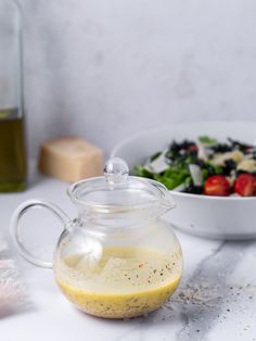 a glass pitcher filled with dressing next to a bowl of salad