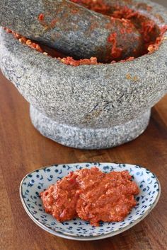 a bowl of red sauce next to a small plate with something in it on a wooden table