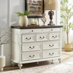 a white dresser sitting in a living room next to a lamp and potted plant