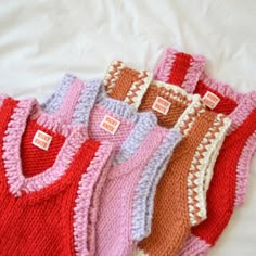 five knitted sweaters are lined up on a white sheet, one is red and the other is pink