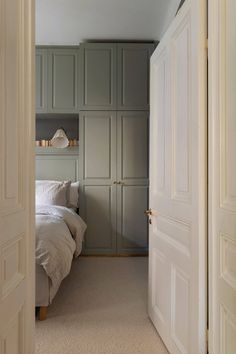 an open door leading to a bedroom with white bedding and green cabinets on either side