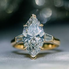 an engagement ring with a pear shaped diamond and baguettes on the side, set in yellow gold