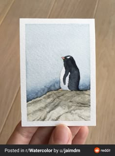 a hand holding up a small card with a penguin on it