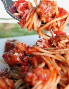 a fork full of spaghetti with meatballs and sauce on the top is being held up