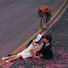 a man and woman sitting on the ground with petals all over them, kissing in front of a bicycle