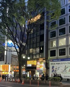 a city street at night with tall buildings and people walking on the sidewalk in front of it