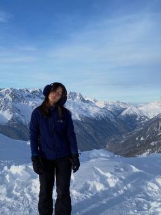 a woman standing on top of a snow covered slope with mountains in the back ground