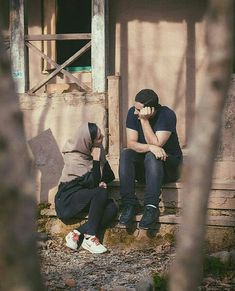 two people are sitting on the steps in front of a building and one is holding his head to his ear