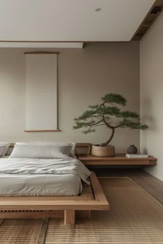 a large bed sitting under a window next to a table with a bonsai tree on it