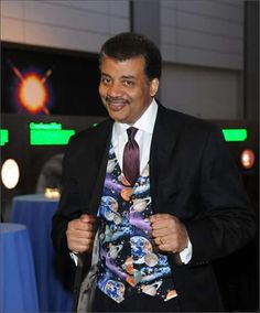 a man in a suit and tie smiles at the camera while standing next to a blue table