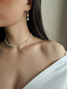 a woman wearing a white top and gold earrings with pearls on the bottom of her neck