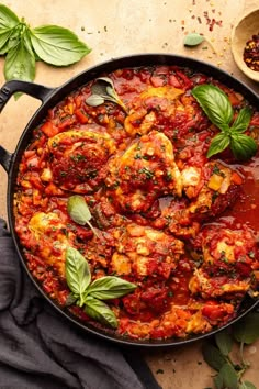 a pan filled with meat covered in tomato sauce and basil leaves on top of a table