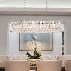 a chandelier hanging over a dining room table with white chairs and flowers on it