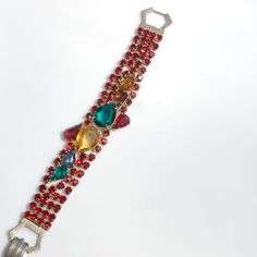 Fabulous Julianna or Julianna style bracelet that features four strands of prong set, deep red rhinestones and a front panel of multicolored, tear-drop shaped stones. The two largest stones have open backs, the rest have closed backs and are foiled. Gold tone metal, fastens securely with a fold-over clasp. Measures 7 1/4 inches long and just under 1 inch at the widest point in the front. The largest stone measures just over 5/8 of an inch by 1/2 of an inch. All the stones are present and in good Red Crystal Rhinestone Bracelet For Party, Red Jeweled Bracelet For Party, Red Rhinestone Crystal Bracelet For Party, Red Crystal Bracelet With Rhinestones For Party, Red Rhinestone Bracelets For Party, Red Crystal Bracelets With Rhinestones, Open Backs, Glamour Photo, Gold And Red