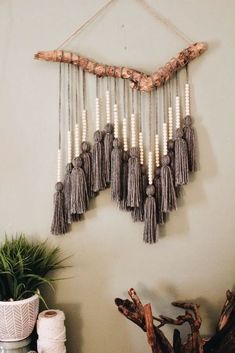 a wall hanging made out of wood sticks and tassels on a white wall next to a potted plant