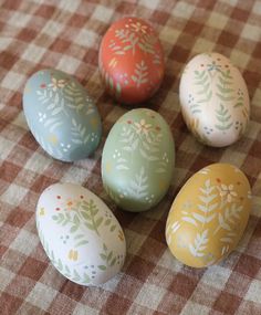 four painted eggs sitting on top of a checkered tablecloth with an inspirational quote