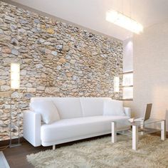 a modern living room with white furniture and stone wall behind the couches, along with a rug on the floor