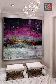 a large painting hanging on the wall in a room with two stools and a chandelier