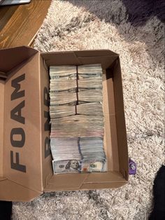 a cardboard box filled with money sitting on top of a carpeted floor next to a pile of cash