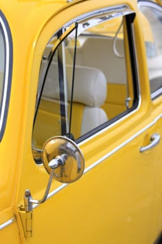 an old yellow car with its door open and the driver's side mirror showing