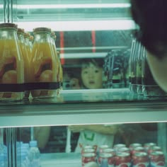 there is a man behind the glass in front of some sodas and orange juice