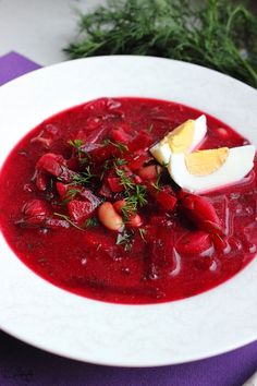 a white plate topped with red soup and an boiled egg on top of the bowl