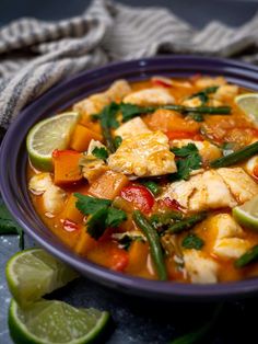 a blue bowl filled with fish and vegetables next to lime wedges on a table