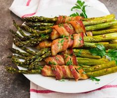 bacon wrapped asparagus on a white plate with a red and white towel next to it