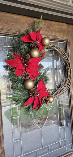 a christmas wreath with poinsettis and pine cones on a front door window