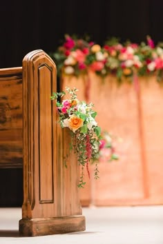 an arrangement of flowers on the back of a wooden church pew during a wedding ceremony