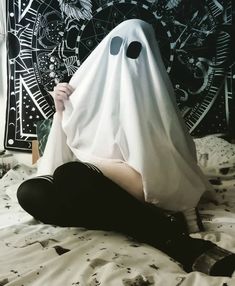 a person in a ghost costume sitting on a bed with a black and white wall behind them