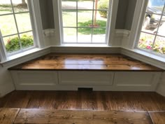 a window seat in the corner of a room with two windows and wood flooring