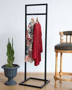 a clothes rack with two coats hanging on it next to a chair and potted plant