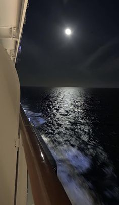 the full moon is seen over the ocean from a ship's deck at night