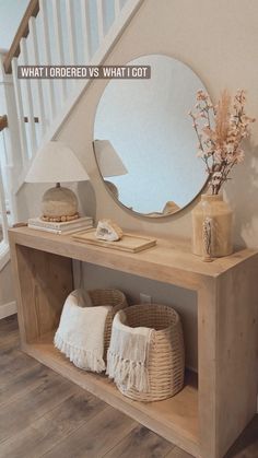 a wooden shelf with baskets and vases on it next to a stair case that has a round mirror above it