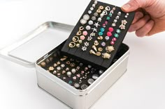 a person holding a metal container filled with lots of different types of rings and earrings