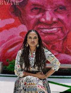 a woman with dreadlocks is sitting in front of a large painting on the side of a building