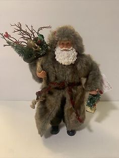 a stuffed santa claus holding a bunch of christmas greenery in his hand and standing on a white surface