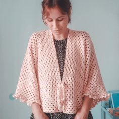 a woman standing in front of a table holding a plate of food and wearing a pink crocheted jacket