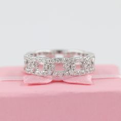 a diamond ring sitting on top of a pink box with a bow tie around it