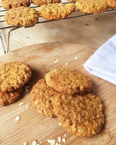 several cookies on a wooden cutting board next to a cooling rack filled with oatmeal