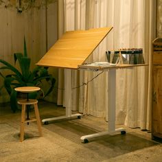 a desk with a wooden top next to a small stool and potted plant on the floor