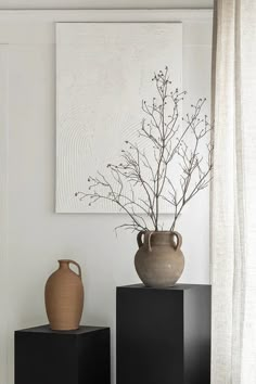 two vases sitting on top of black boxes in front of a painting and window