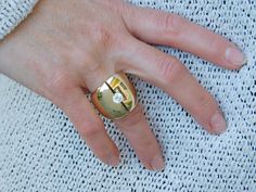 a woman's hand with a gold ring on top of her finger and a white sweater