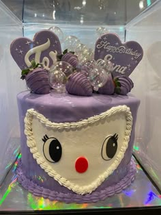 a birthday cake with purple frosting and decorations on it's face is displayed in a glass case