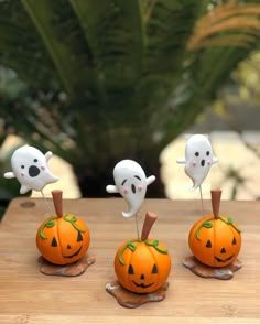 three pumpkins with ghost faces on them sitting on top of a wooden table next to a potted plant