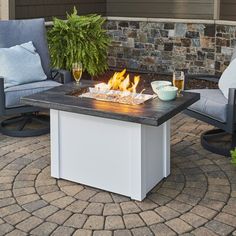 a fire pit sitting on top of a patio next to two chairs and a table